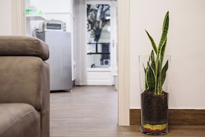 Ein Wohnzimmer mit einem braunen Sofa, einer Glasvase mit Pflanze und einer Küchenzeile im Hintergrund.