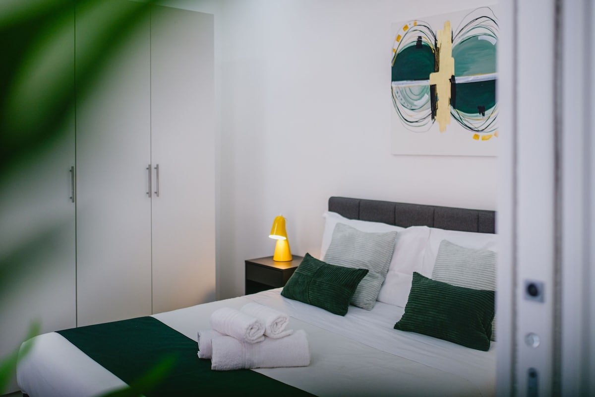 Ein ordentlich bezogenes Bett mit Kissen, einer Nachttischlampe und einer grünen Tagesdecke.