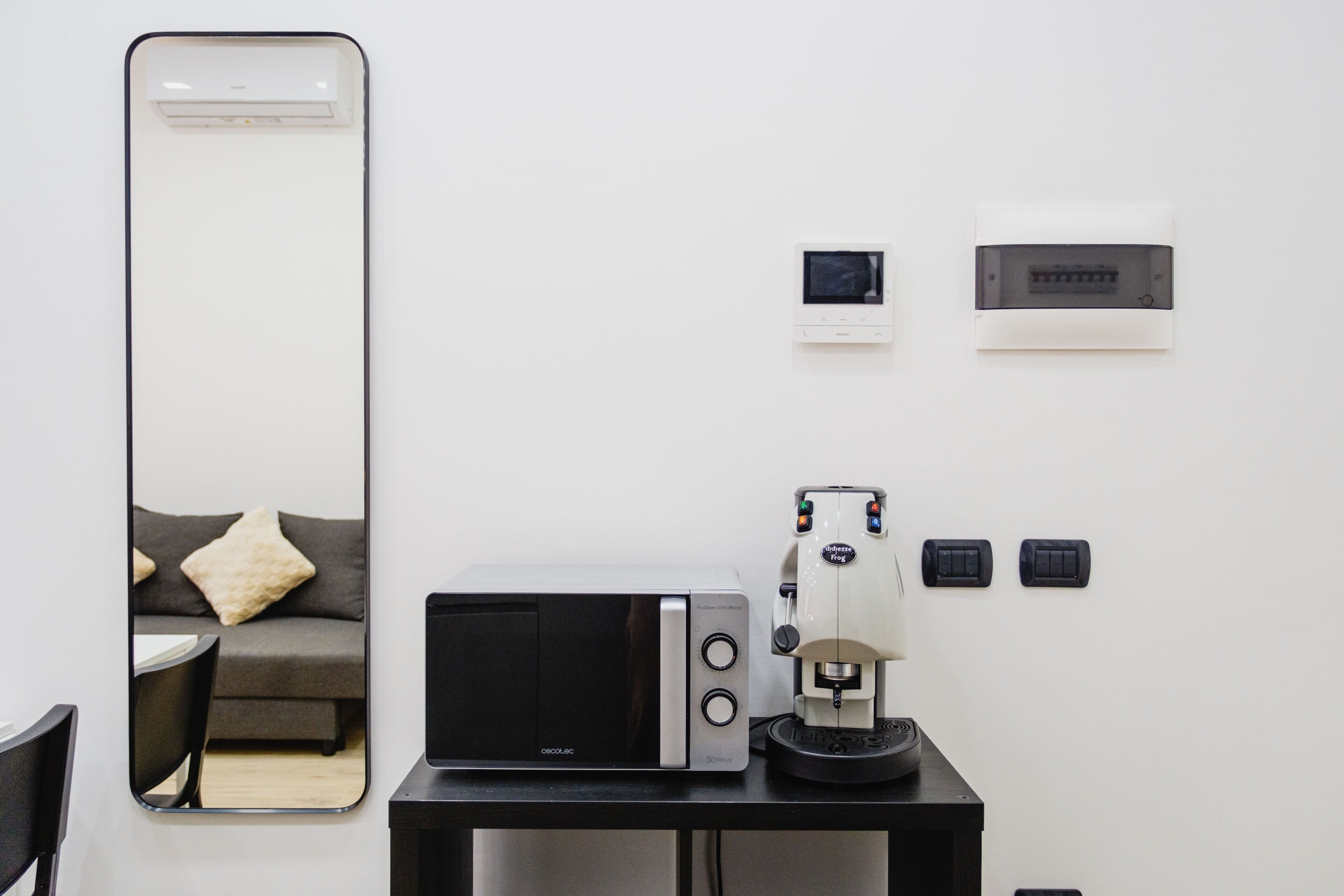 Una camera moderna con uno specchio grande, un forno a microonde, una macchina per il caffè e un tavolino.