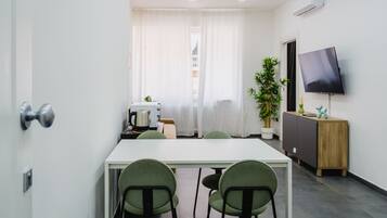 A modern room with a white table, green chairs, a TV, a plant, and a cabinet.