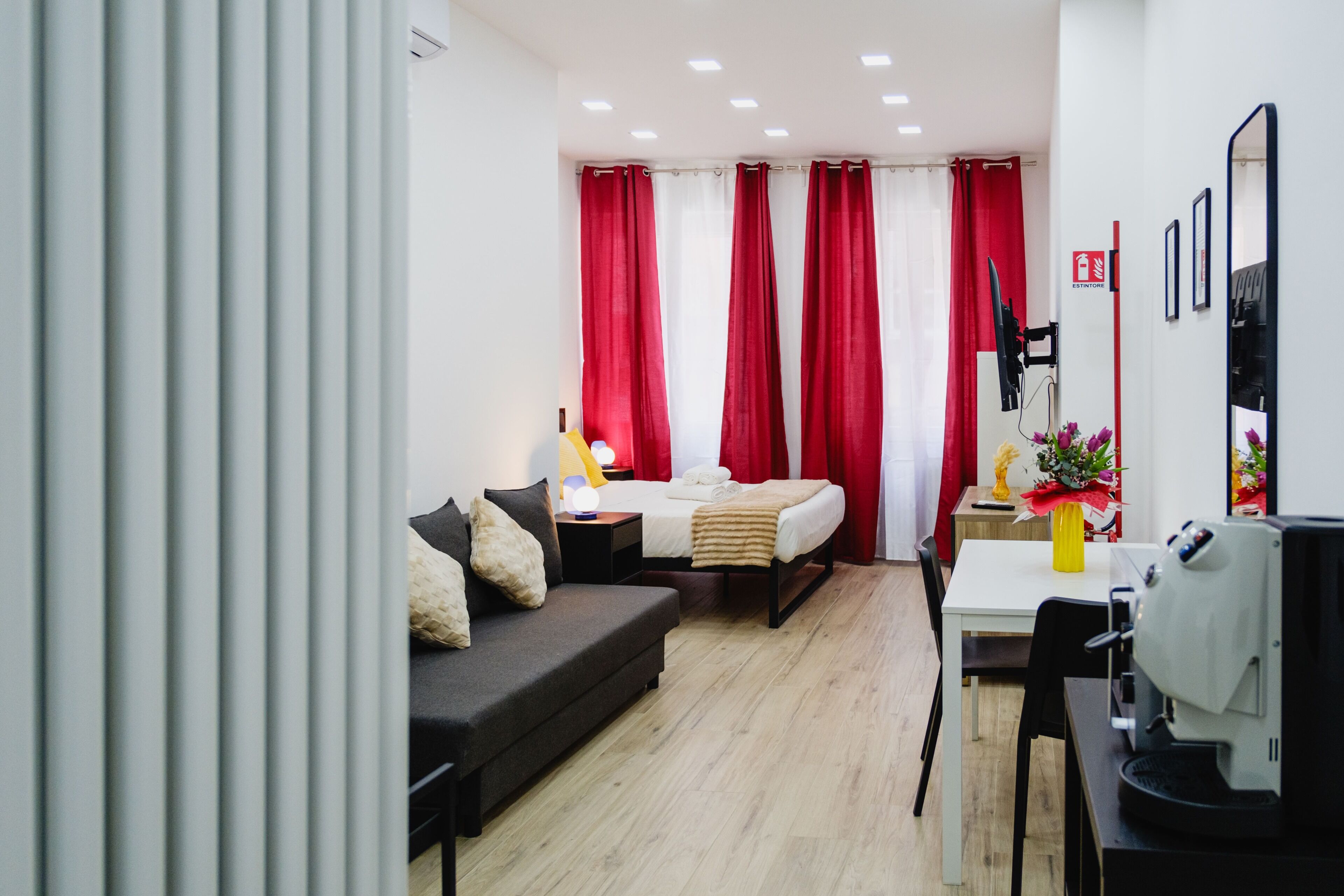 Ein modernes Hotelzimmer mit Bett, Sofa, Esstisch und einer Kaffeemaschine.