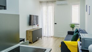 A modern living room with a flat-screen TV, a wooden cabinet, a sofa with cushions, a small table, and a potted plant. - Via Niccolò Tommaseo 4 - Appartamento 4 (Naples)