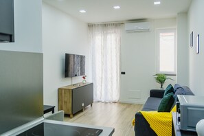 Ein modernes Wohnzimmer mit Flachbildfernseher, einem Holzkasten, einer Couch mit Kissen, einem kleinen Tisch und einer Topfpflanze.