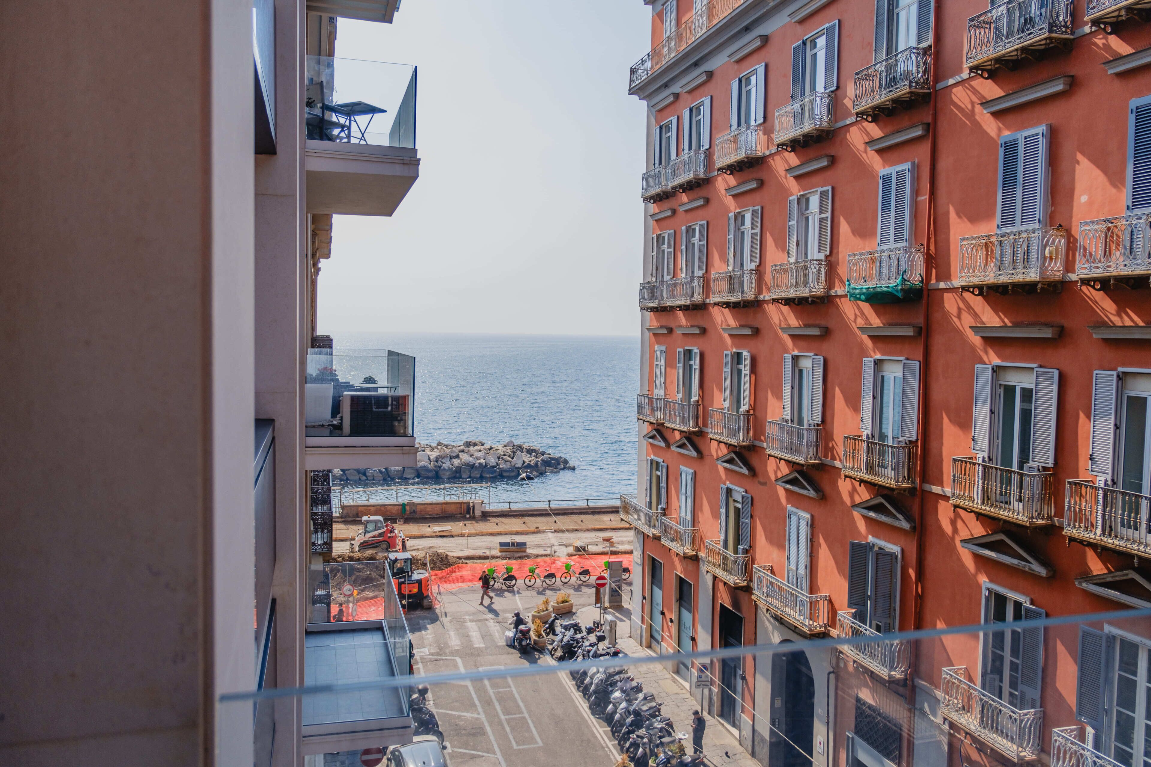 Un edificio a più piani con balconi, vista sul mare e una strada con motociclette parcheggiate.