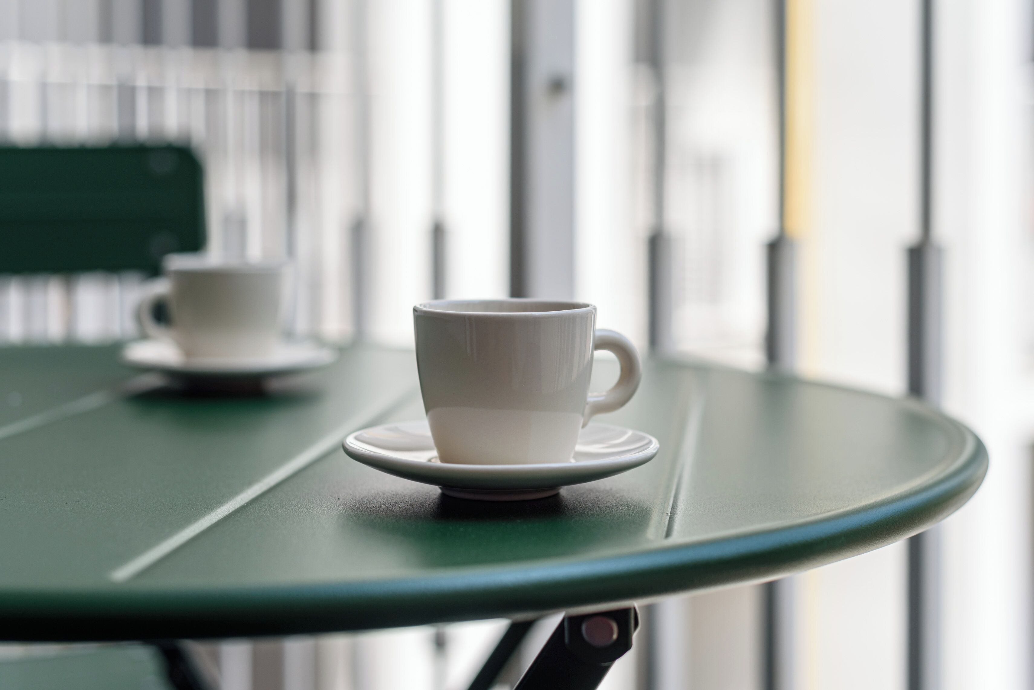 A close-up of a white cup on a green table with a blurred background.