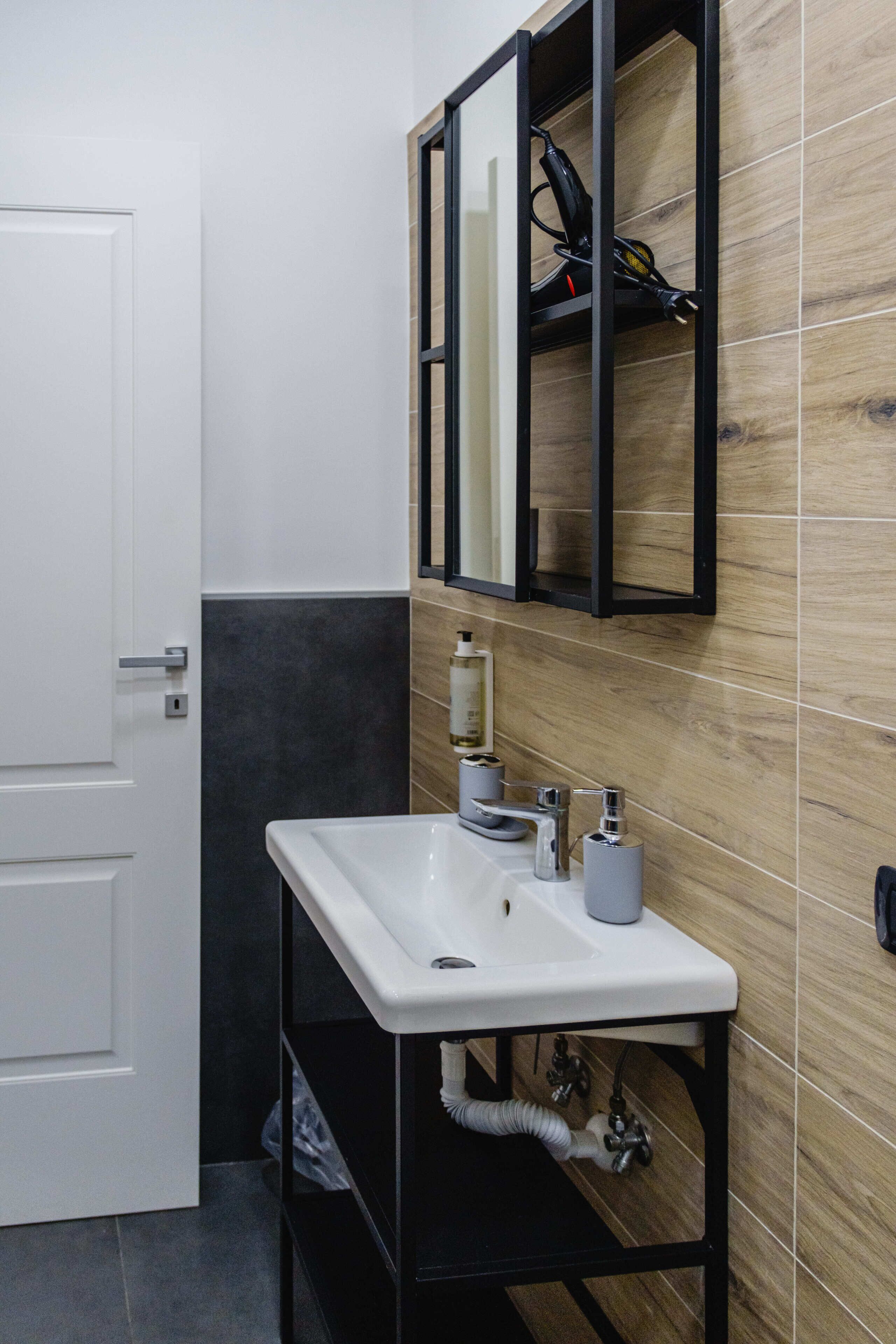 Un baño con un lavabo blanco, estanterías negras y un espejo.