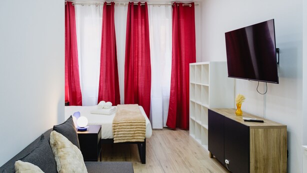 A hotel room with a bed, a sofa, a TV, a bedside table with a lamp, and a cabinet. - Via Niccolò Tommaseo 4 - Appartamento 4 (Naples)