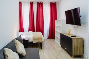 A hotel room with a bed, a sofa, a TV, a bedside table with a lamp, and a cabinet. - Via Niccolò Tommaseo 4 - Appartamento 4 (Naples)