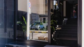 A modern building entrance with glass doors, a visible parking sign, and a staircase leading inside.