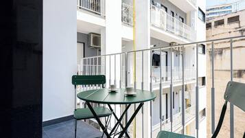 A balcony with a glass table and chairs, overlooking a building with multiple balconies and railings.