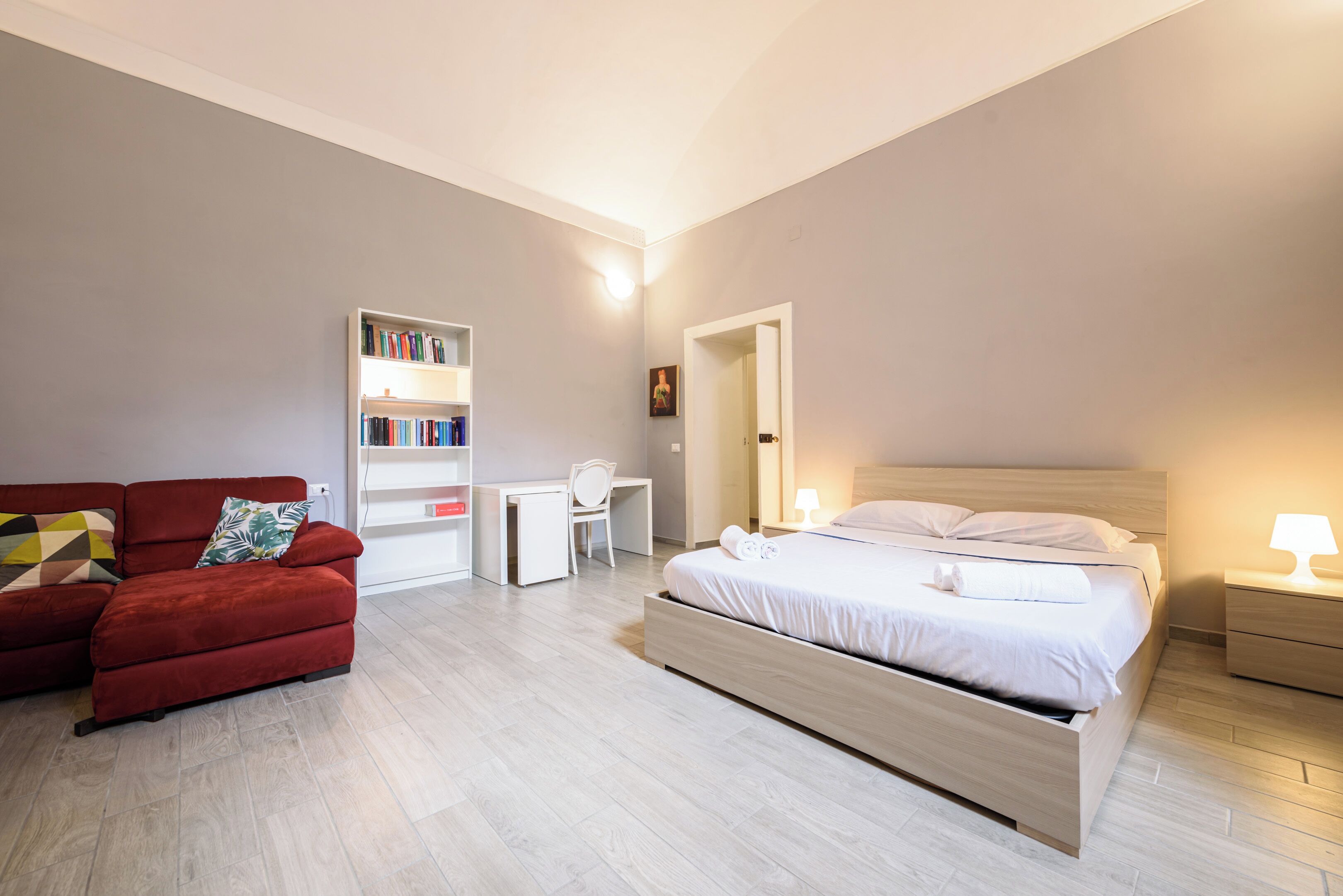 A modern bedroom with a bed, a red sofa, a bookshelf, and a desk.