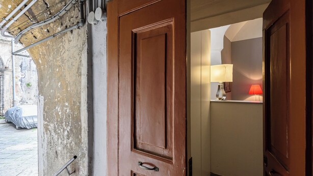 A wooden door leading to a room with a lamp and a bed. - Via Atri 37 (Naples)