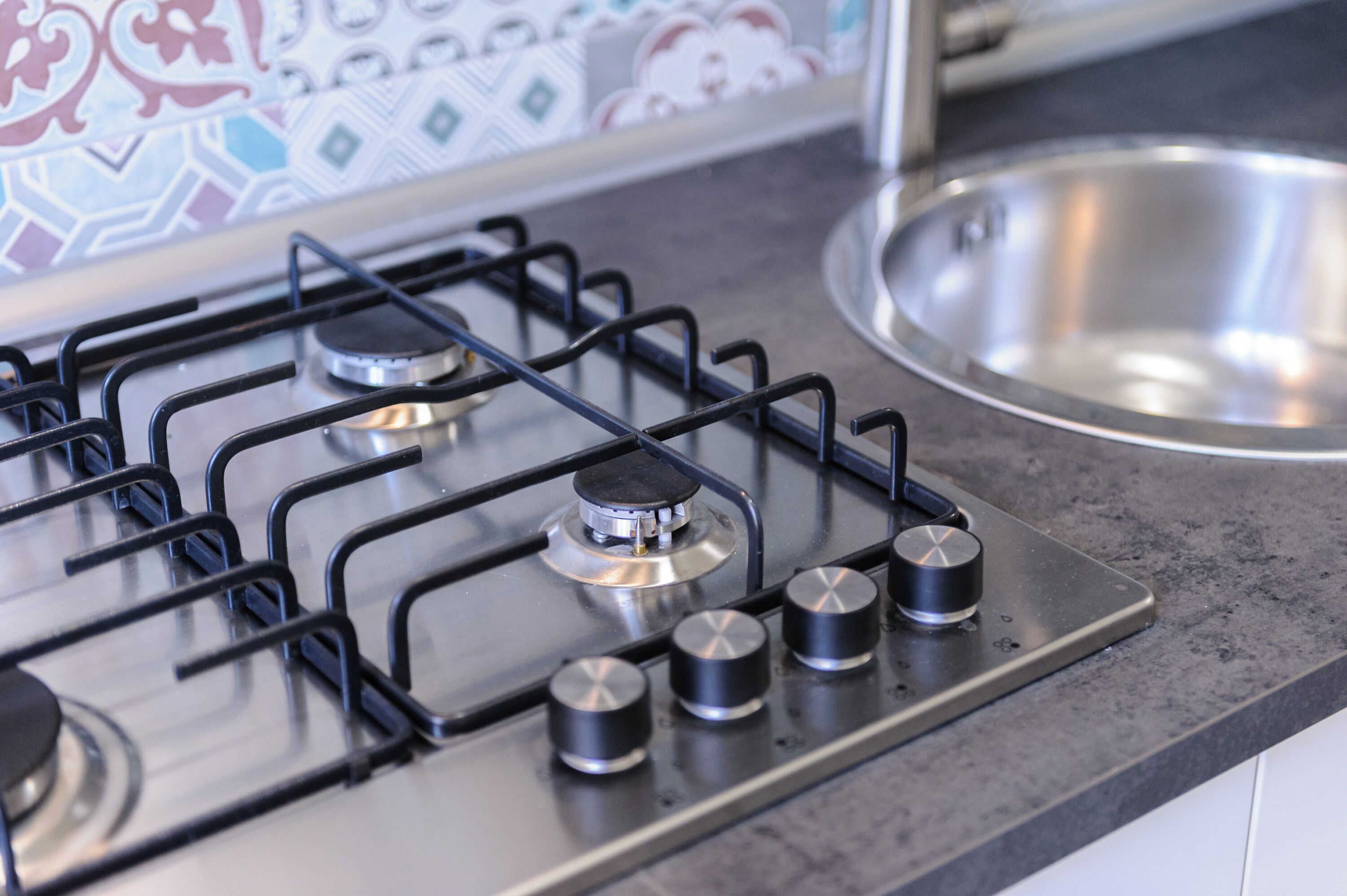 Una cocina con estufa a gas, pileta de acero inoxidable y salpicadero de azulejos.