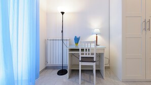 Ein kleiner, gut beleuchteter Raum mit Schreibtisch, Stuhl, Stehlampe und Schrank.