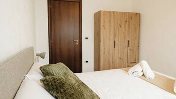 A bedroom with a bed, a wooden wardrobe, a door, and a nightstand with a lamp.