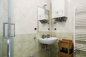 Un baño con cabina de ducha de vidrio, un lavamanos blanco, un espejo y un perchero para toallas.