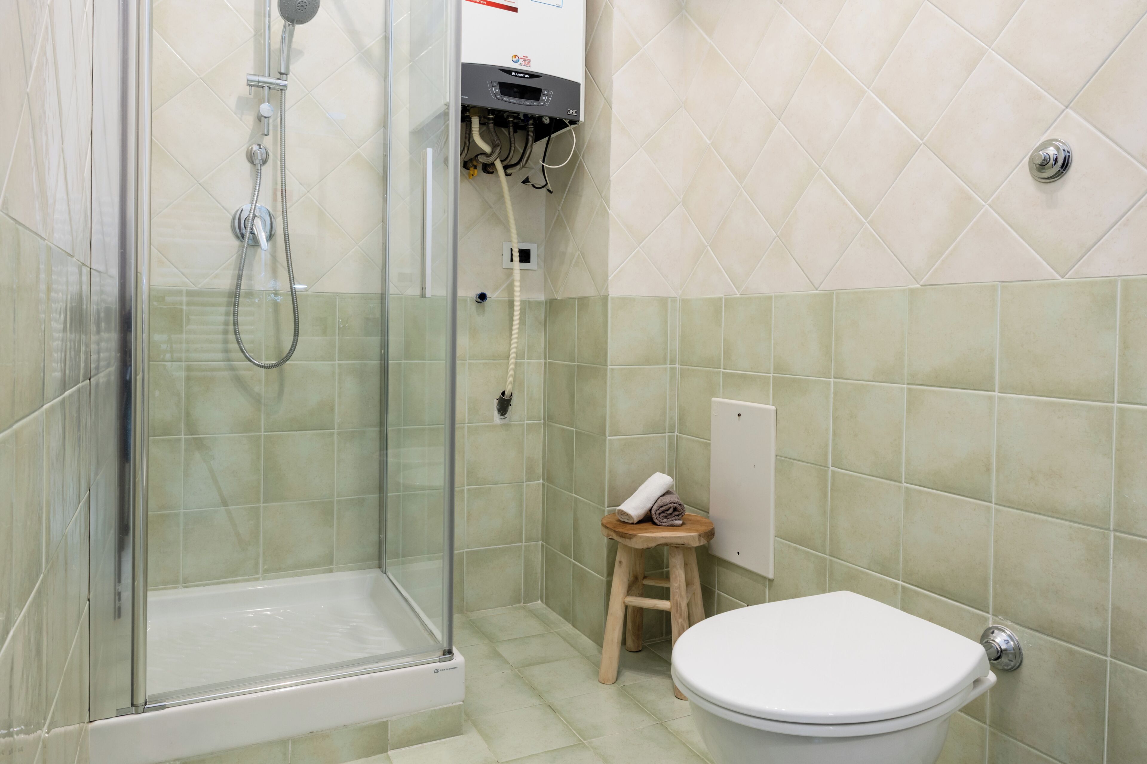 Un bagno con doccia vetrata, un water e un piccolo sgabello di legno.