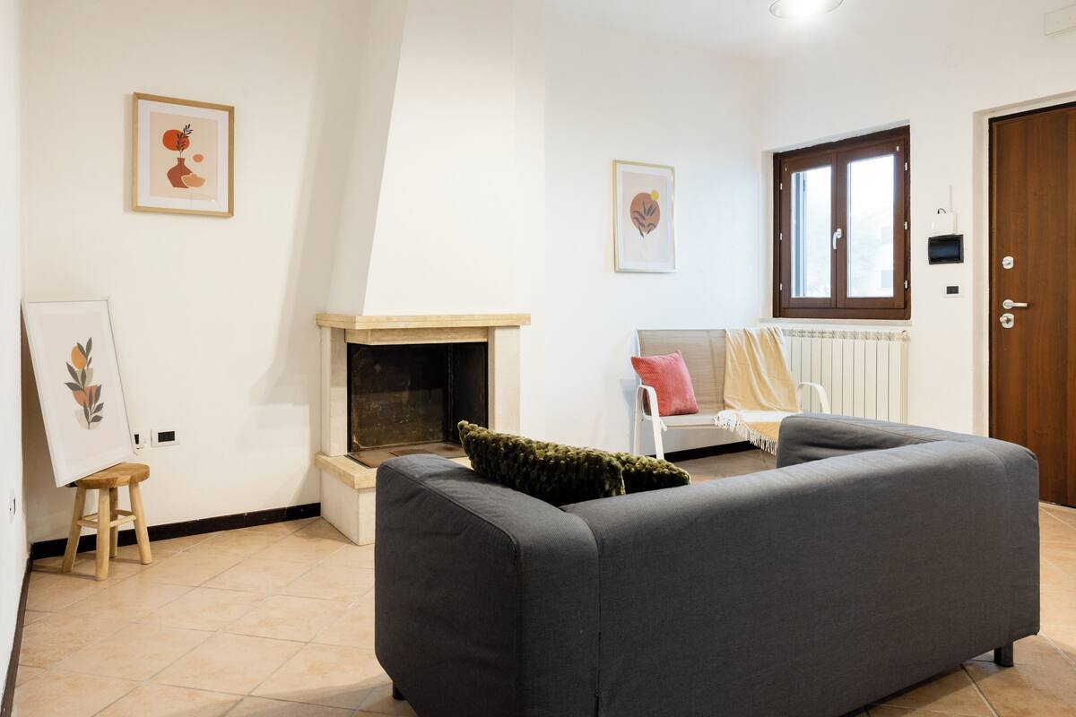 Una sala de estar con chimenea, un sofá, una silla y obras de arte en las paredes.