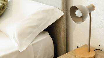 Una cama con ropa blanca, una mesita de noche con lámpara y una mesita auxiliar de madera.