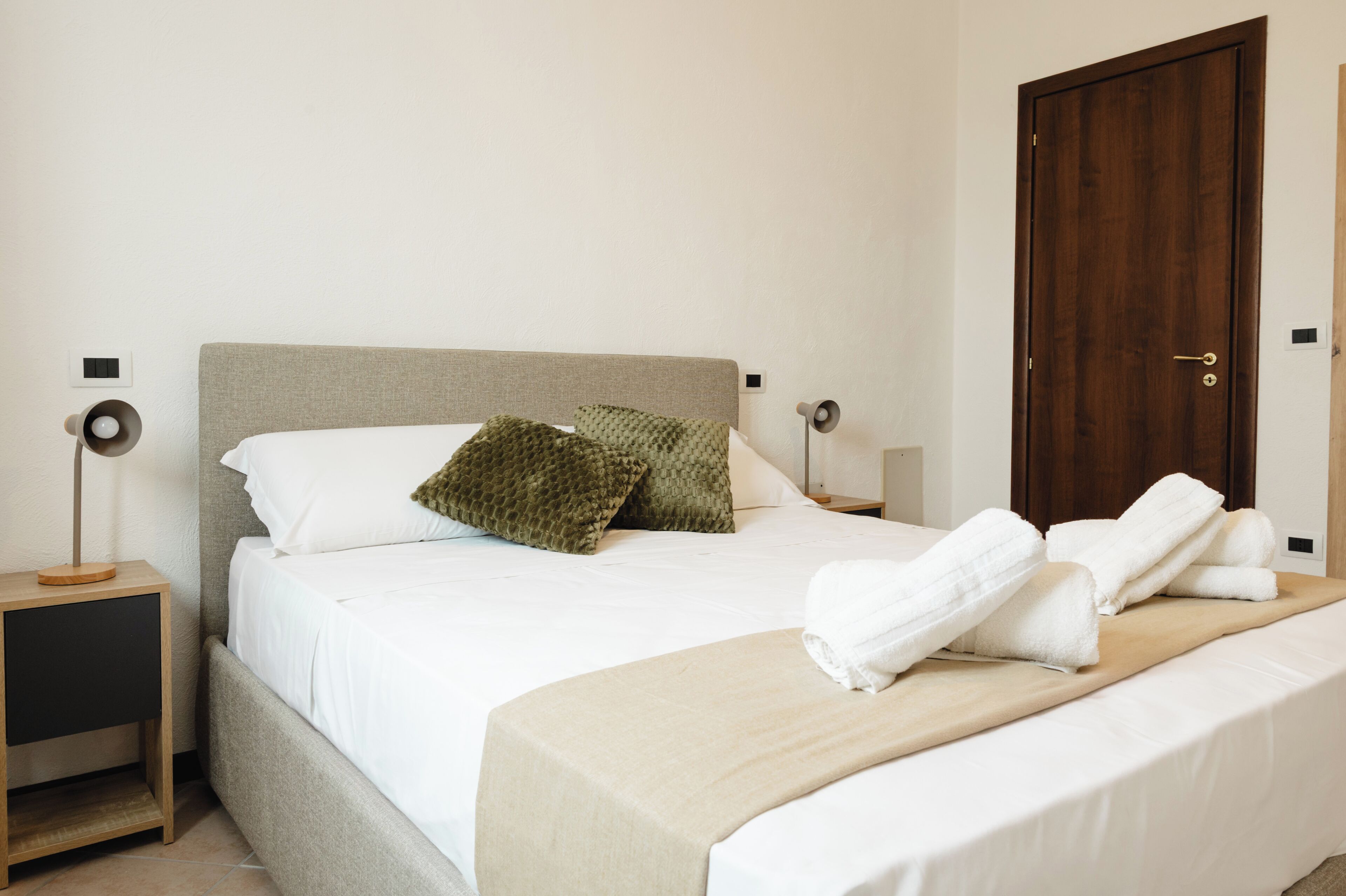 Un letto rifatto con cuscini, una lampada da comodino e una porta in legno in una camera d'albergo.
