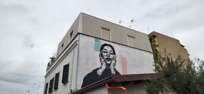 A building with a mural of a person on the side, antennas on the roof, and a tree in the foreground. - La Casetta con Giardino al Pigneto (Rome)