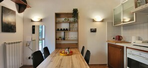 A compact kitchen with a wooden table, black chairs, a fruit tray, and a built-in shelf with kitchenware. - La Casetta con Giardino al Pigneto (Rome)