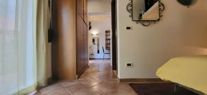 A hallway with a bed on the right, a door on the left, and a mirror on the wall. - La Casetta con Giardino al Pigneto (Rome)