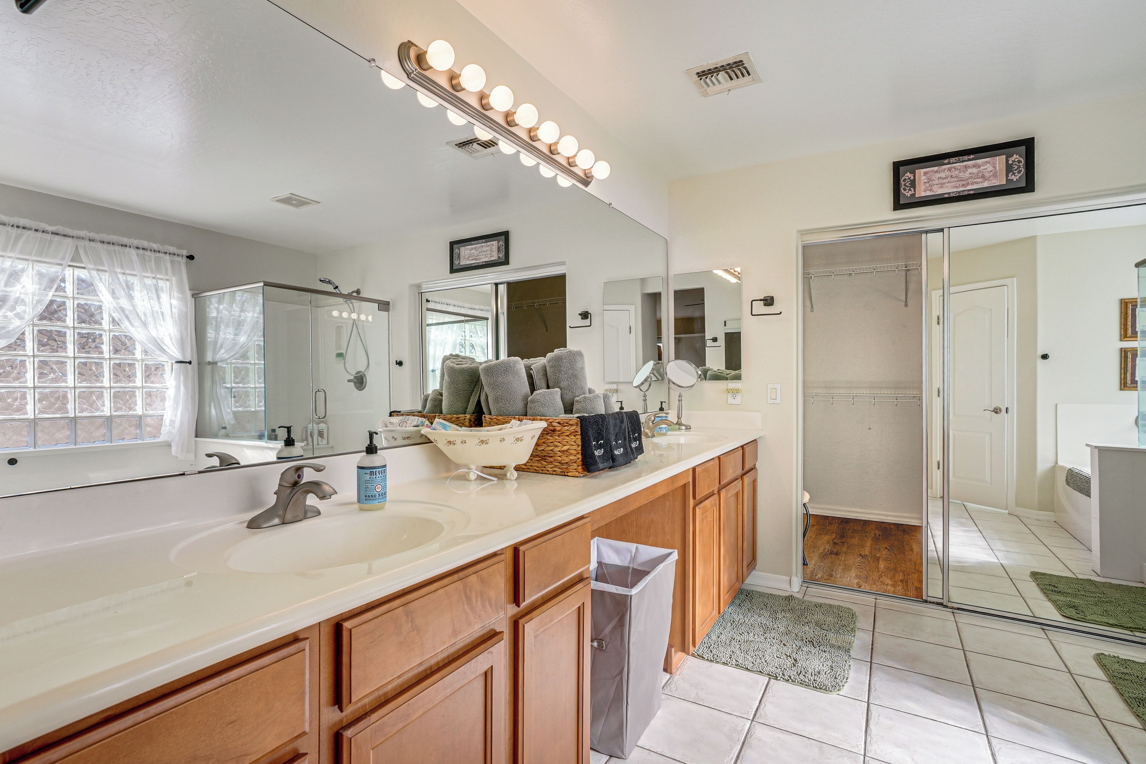 A bathroom with a large mirror, vanity, sink, and shower.