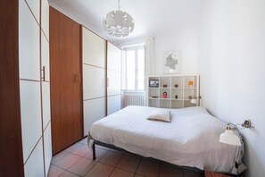 Ein Schlafzimmer mit Bett, Kleiderschrank, einer Ablage mit Dekoration und einem fenster mit Vorhängen.