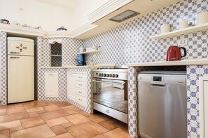 Una cocina equipada con refrigerador, horno y lavavajillas. Presenta baldosas decorativas en las paredes y piso de baldosas.