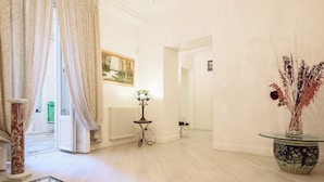 Ein geräumiges Zimmer mit großem Fenster, Heizkörper, kleinem Tisch mit Lampe und dekorativer Vase mit Trockenpflanzen.