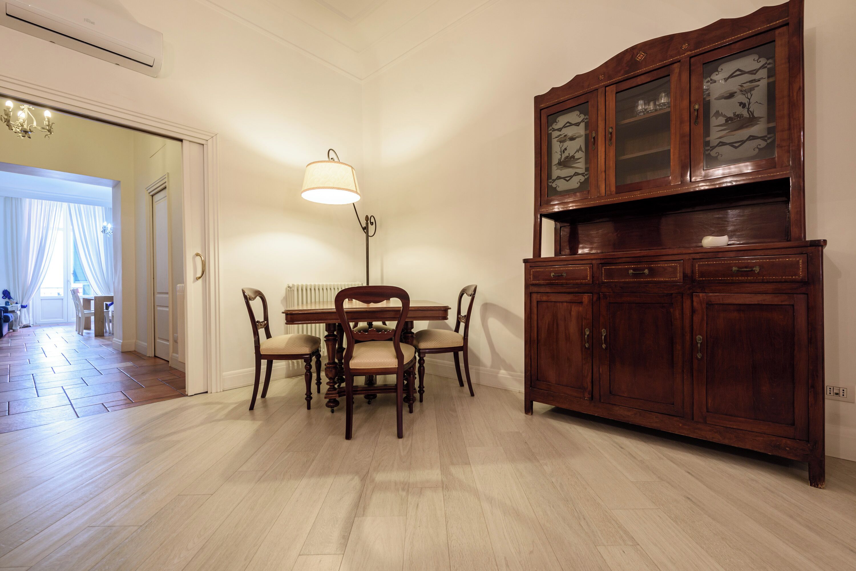 Un coin repas avec une table et des chaises en bois, une lampe et un meuble avec des portes en verre.