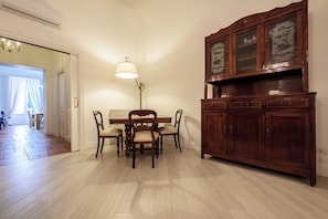 A dining area with a wooden table and chairs, a lamp, and a cabinet with glass doors. - Palazzo Dello Spagnolo Suite (Naples)