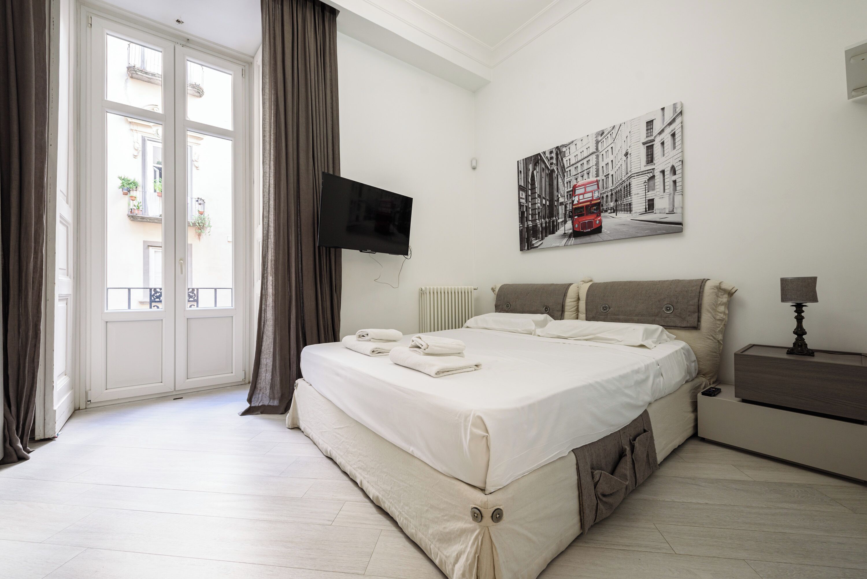 Een slaapkamer met een bed, een televisie, een nachtkastje en een raam met gordijnen.