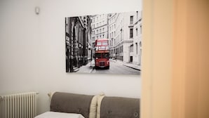 Ein Hotelzimmer mit einem Doppelbett, einem Heizkörper und einem an der Wand befestigten Bild eines roten Doppeldeckerbusses auf einer Stadtstraße.