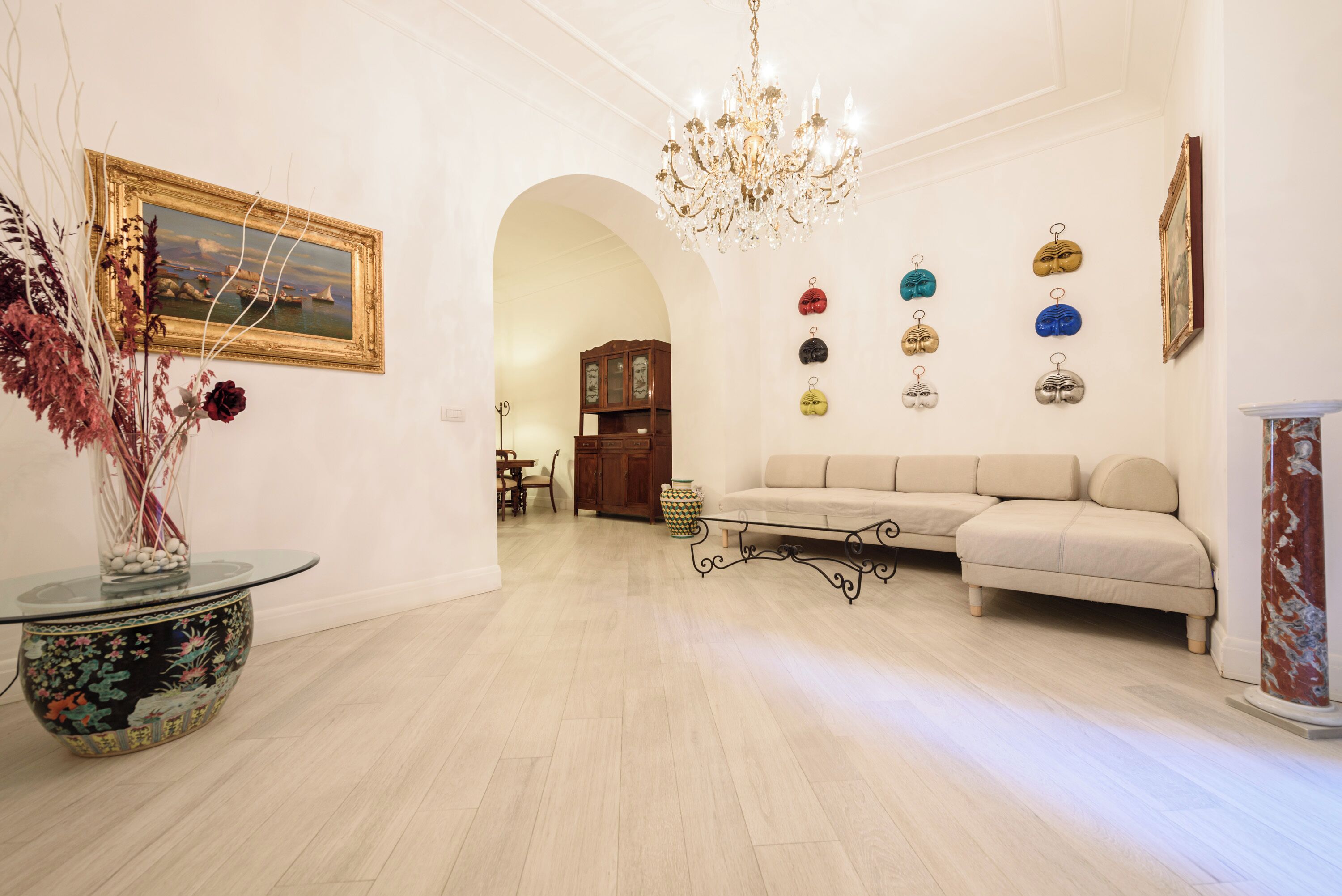 Een ruime woonkamer met een bank, een kroonluchter en een wand met decoratieve objecten.
