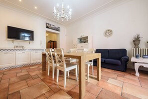 Una sala de estar con televisor, mesa de comedor, sillas, sofá y una araña.
