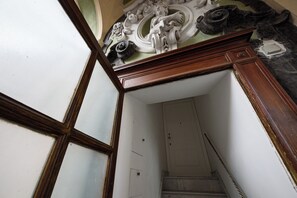 Una escalera que conduce a una puerta blanca, un marco de madera y un techo decorado con diseños intrincados.