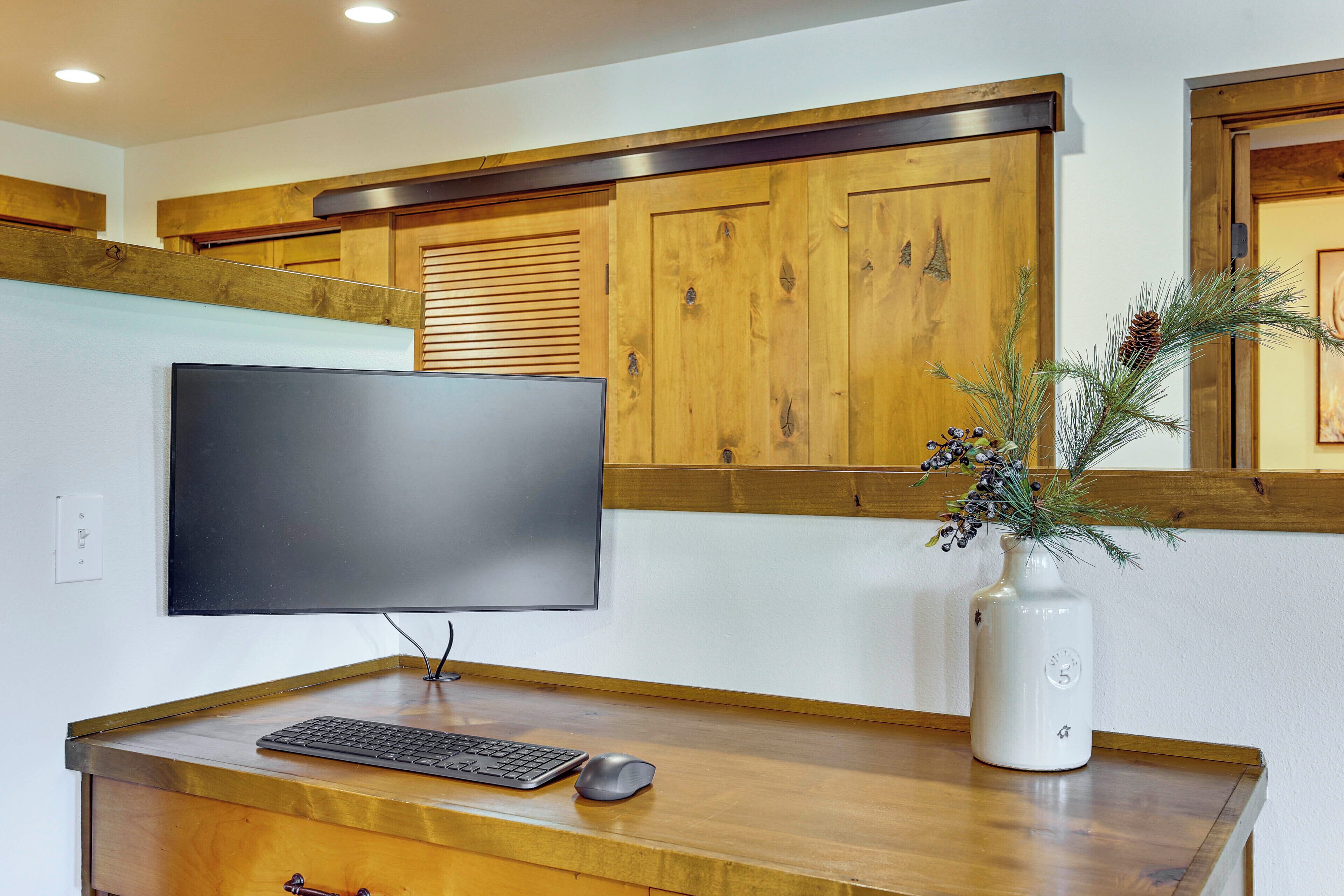 A modern office desk with a computer, keyboard, and mouse, a flat-screen monitor, a wooden cabinet, and a decorative vase with pine branches.