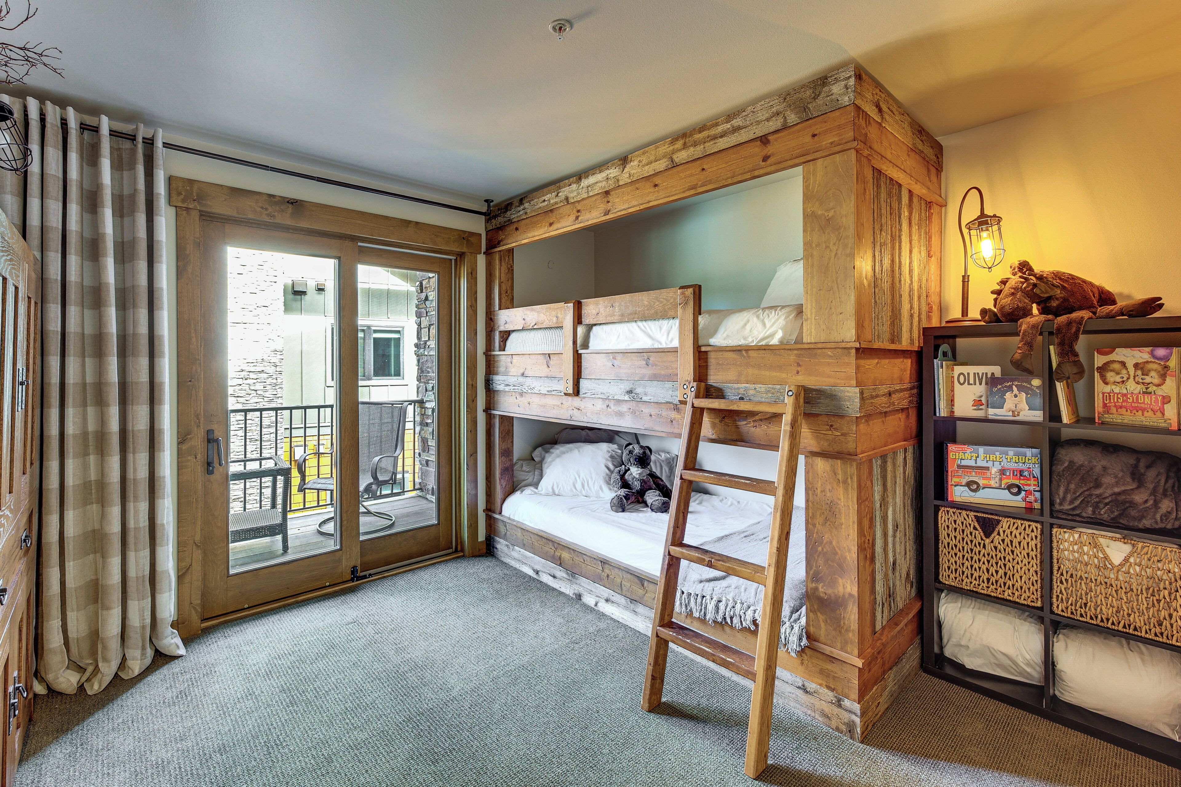 A room with a bunk bed, a ladder, a bookshelf, and a sliding glass door leading to an outdoor area.