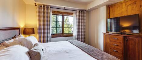 A hotel room with a bed, a TV on a wooden cabinet, a window with curtains, and a lamp.