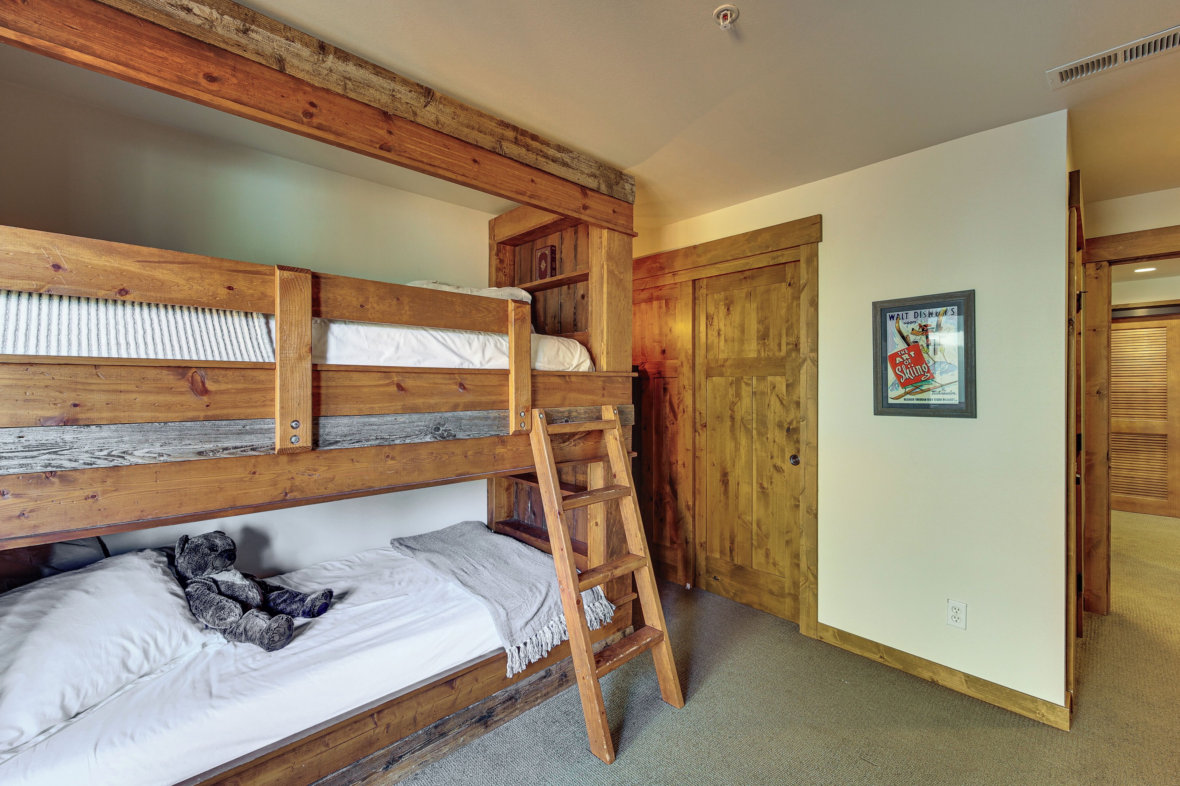 A bunk bed with a ladder, a teddy bear, and a poster on the wall.