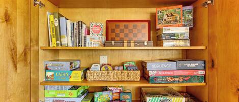 A wooden cabinet with shelves containing various board games and puzzles.