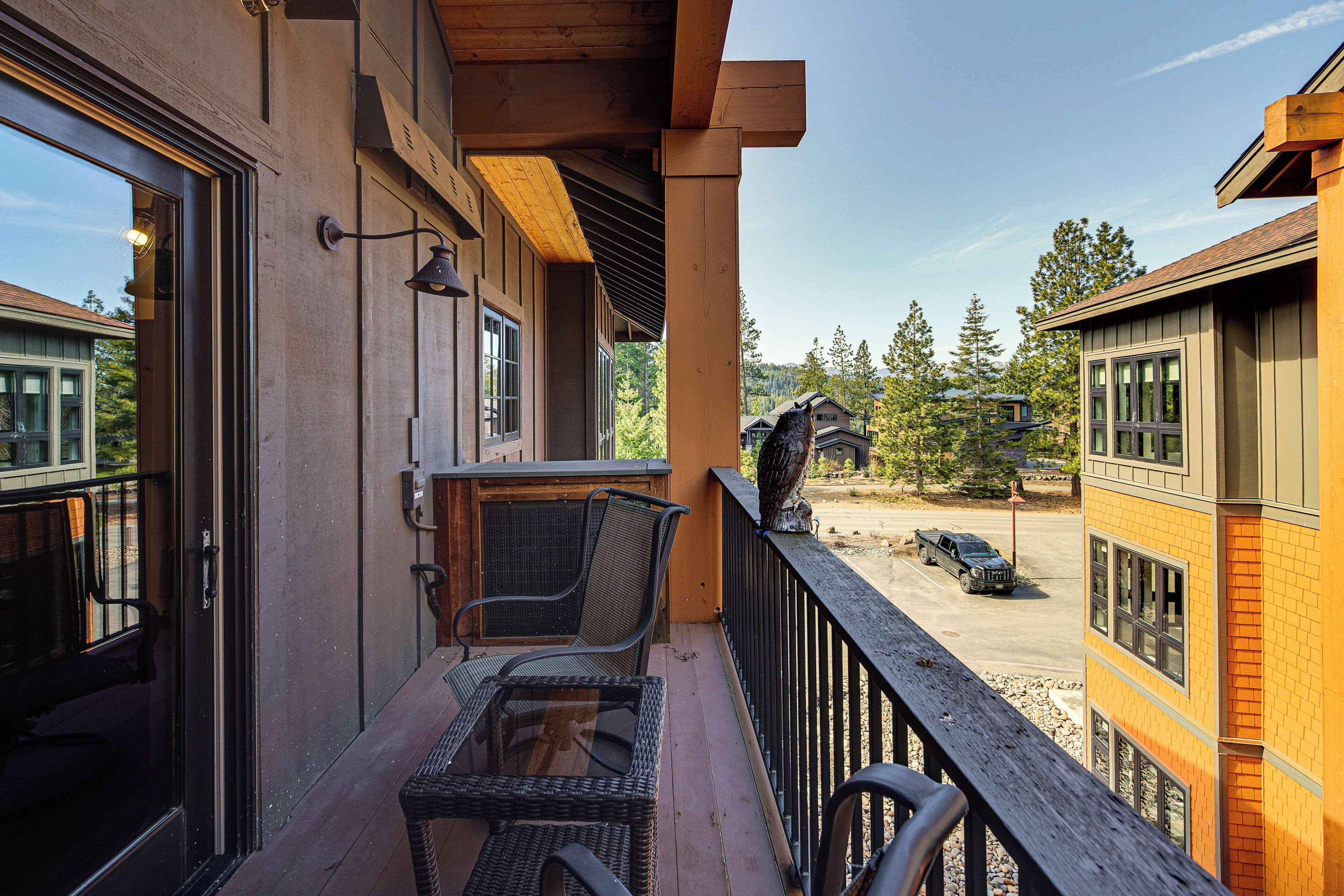 A balcony with wicker furniture, a wooden railing, and a view of a parking area and neighboring buildings.