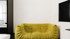 Uma poltrona de pelúcia amarela num quarto moderno com uma cama e uma televisão na parede.