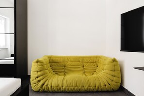 A yellow bean bag chair in a modern room with a bed and a TV on the wall. - Kobogaisha (Rome)