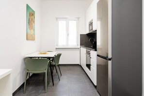 A compact kitchen with a dining table, chairs, a window, and modern appliances. - Kobogaisha (Rome)