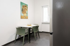 A dining area with a white table, two green chairs, a bowl, and a painting on the wall. - Kobogaisha (Rome)