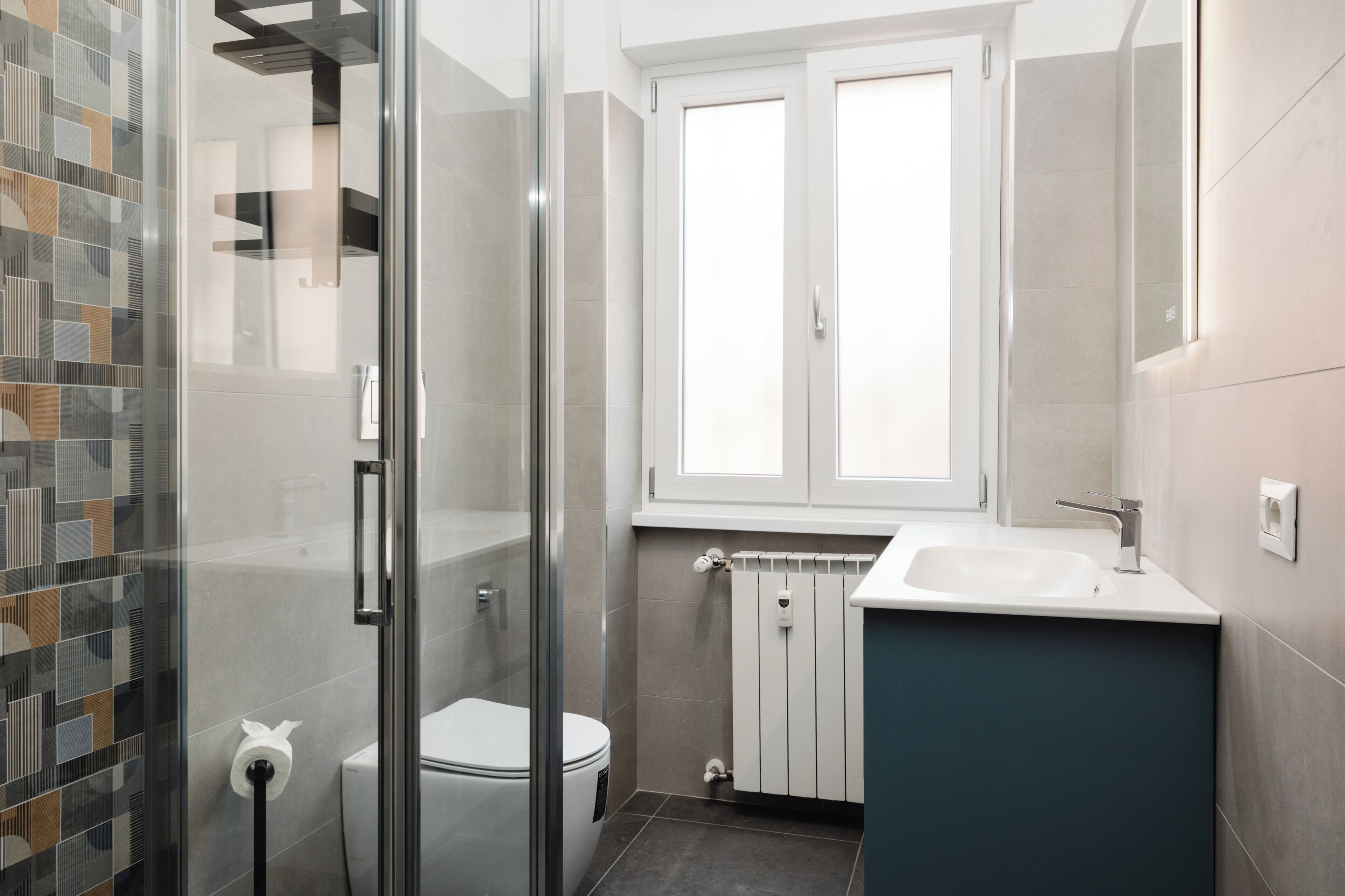 A modern bathroom with a glass shower enclosure, a toilet, a sink, and a window above the mirror.