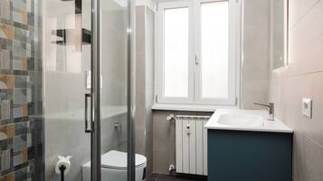 A modern bathroom with a glass shower enclosure, a toilet, a sink, and a window above the mirror.